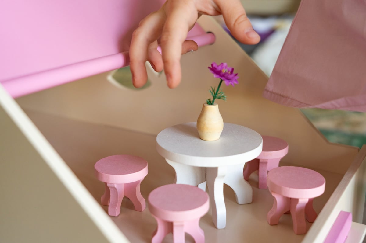A child's hand arranging miniature wooden furniture inside a dollhouse